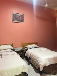 two beds in a room with a red wall at Homestay Tok Penghulu in Kuantan
