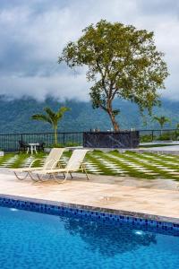 a swimming pool with two chairs and a tree at SaffronStays Sundowner by the Lake, Karjat - party-perfect pool villa with rain dance and cricket turf in Karjat