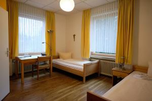 a room with a bed and a desk and two windows at St. Bonifatiuskloster - Geistliches Zentrum in Hünfeld