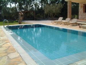 a large blue swimming pool with chairs and a house at Villa Karissa - Zante in Vasilikos