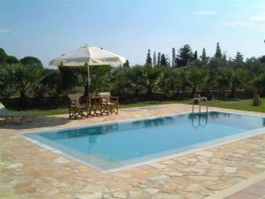 a swimming pool with an umbrella and a table at Villa Karissa - Zante in Vasilikos