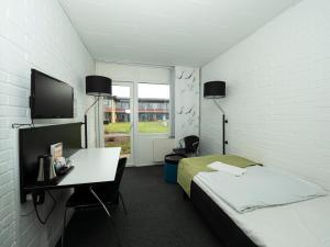 Kobæk Strand Konferencecenter في Skælskør: غرفة بها سرير ومكتب وتلفزيون