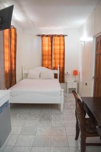 a bedroom with a white bed with orange curtains and a desk at St. James Guesthouse in Roseau