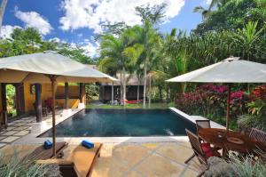 a swimming pool with two umbrellas next to a house at Jendela Di Bali Villa in Tegalalang