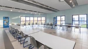 Heudicourt-sous-les-CôtesにあるHébergements du Lac de Madineの窓のある部屋にテーブルと椅子が置かれた教室