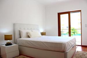 a white bedroom with a large bed and a window at Damaia Apartment in Amadora