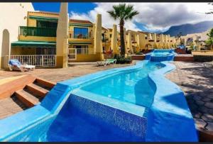 a blue swimming pool in front of a building at Luxury Apartment fronte piscina Mareverde A&V Costa Adeje in Adeje