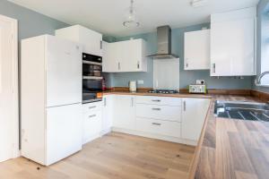 a kitchen with white cabinets and a wooden floor at 4 Bedroom Detached House 5mins walk to shopping village in Bicester