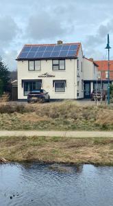 une maison avec des panneaux solaires à côté d'une masse d'eau dans l'établissement Pension Brinkvis, à De Koog