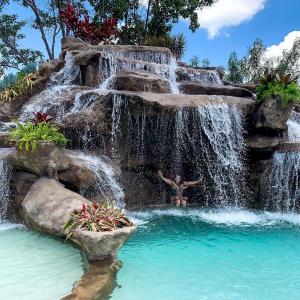 a waterfall in a pool with a person in it at Lara's Home Suites in Capitólio