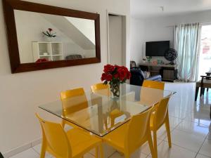 uma mesa de vidro com cadeiras amarelas e um vaso de flores vermelhas em Condomínio Portal de Maragogi- Flats duplex super aconchegantes e confortáveis em Maragogi