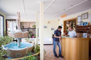 deux hommes debout à un comptoir dans un magasin dans l'établissement Hotel Panorama e Residence, à Tremosine