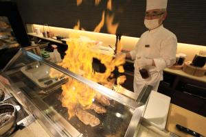 a chef cooking meat on a grill in a kitchen at Matsunoi in Minakami