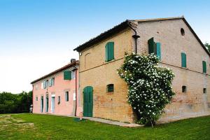 um grande edifício de tijolos com portas verdes e um arbusto em Holiday home Casale le Fontanelle, Monterado em Monterado