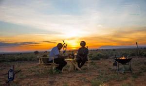 Un uomo e una donna seduti a un tavolo di fronte al tramonto di Amanya Double Pitch Tent with Mt Kilimanjaro View ad Amboseli
