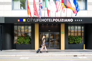 uma mulher andando em frente a um edifício com bandeiras em City Life Hotel Poliziano, by R Collection Hotels em Milão