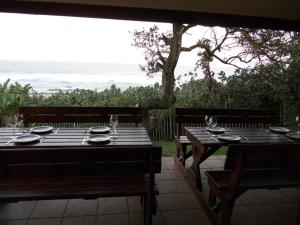 een tafel met borden en wijnglazen op een patio met uitzicht op de oceaan bij Shore Breakers in Shelly Beach