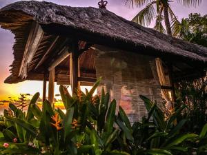 a house with a straw roof and some plants at Santai Hotel in Amed