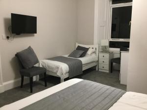 una camera con 2 letti, una sedia e una TV di Amaryllis Guest House a Edimburgo