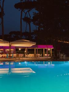 una grande piscina di notte con tavoli e ombrelloni di ISOLA VERDE Camping Village a Nettuno