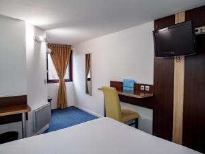 Cette chambre comprend un lit, un bureau et une télévision. dans l'établissement Contact Hotel Restaurant La Chaumière Les Mureaux-Flins, aux Mureaux