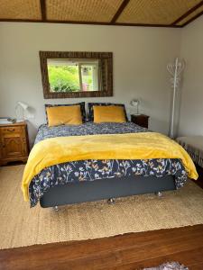 a bedroom with a bed with a yellow blanket and a mirror at Sundari Retreat in Otaki