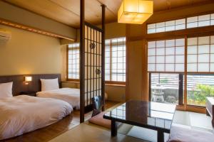 two beds and a table in a room with windows at Toushinan Komeya in Ito