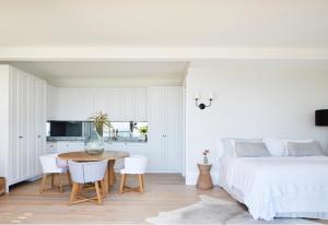 a white bedroom with a bed and a table and chairs at The Cape at Wategos Pool Pavilion in Byron Bay