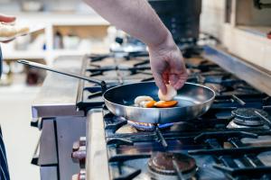 a person cooking food in a pan on a stove at The Corrie Hotel in Corrie