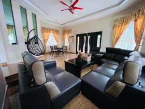 a living room with black leather furniture and a ceiling fan at Homestay Seri Pangkor in Pangkor