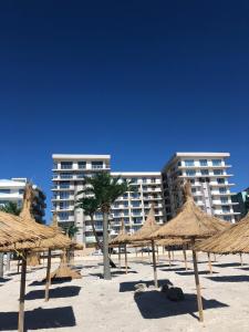 eine Gruppe Strohschirme an einem Strand mit einem Gebäude in der Unterkunft Bakuba - Studio pe plaja cu vedere la mare & loc parcare gratis in Mamaia Nord – Năvodari