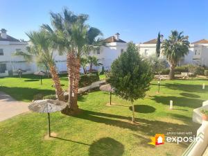 a park with palm trees in front of a building at Casa adosada con porche, piscina y pista de pádel, junto al campo de golf in El Portil