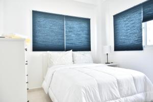 a white bedroom with a white bed and blue blinds at Apartamento en Juan Dolio Tepuy 501 B in Juan Pedro