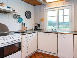 ヘンネ・ストランドにあるHoliday Home Hyttestienの白いキャビネットと壁掛け時計付きのキッチン