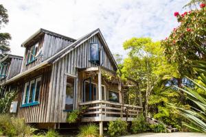 Casa de madera con ventanas azules y árboles en Fern Lodge Coromandel en Coromandel Town