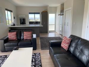 a living room with two black leather couches at Mahina Cottage in Twizel