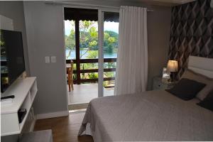 1 dormitorio con 1 cama y puerta a un balcón en Mirante da Figueira - Suítes para temporada, en Angra dos Reis