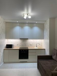 ブチャにあるАпартаменти в ЖК Гранд Бурже подобовоの白いキャビネット、シンク、ソファ付きのキッチンが備わります。