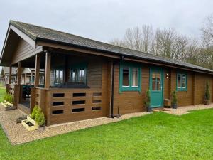 eine Holzhütte mit grüner Tür und Gras in der Unterkunft Heron Lodge, Lake Pochard in South Cerney