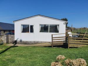 a small white house with a wooden fence at On farm Chalet, sleeps 6, Rhoshirwaun in Aberdaron
