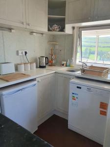 a kitchen with white cabinets and a white dishwasher at On farm Chalet, sleeps 6, Rhoshirwaun in Aberdaron