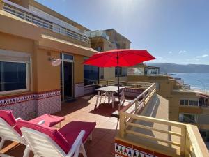 balcón con mesa, sillas y sombrilla roja en Los Gueldes, en Las Palmas de Gran Canaria