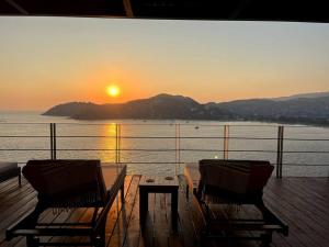 two chairs and a table on a deck with the sunset at El Nido Casa 4 - Paradise on the Bay in Zihuatanejo