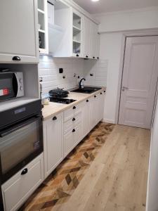 a kitchen with white cabinets and a wooden floor at Neversea Apartment in Constanţa