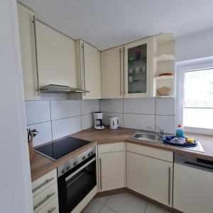 eine Küche mit weißen Schränken, einem Waschbecken und einem Fenster in der Unterkunft Wohnung "Orther Hafen" in Bannesdorf auf Fehmarn in Fehmarn