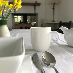 un tavolo con una tazza di caffè bianco e cucchiai di Uplands Garden a Morecombelake