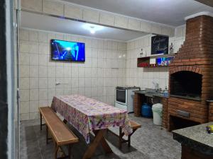 a kitchen with a table and a tv on a wall at Casa grande e confortável até 16 pessoas com churrasqueira e garagem para 8 carros in Praia Grande