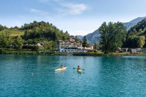 two people kayaking on a lake in front of a house at Panoramic Hotel San Carlo Ledro in Ledro