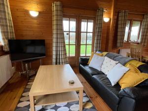 a living room with a black leather couch and a table at Kingfisher Lodge, Lake Pochard in South Cerney