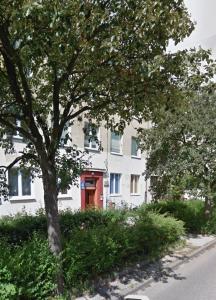 a white building with a red door next to a tree at Przytulne mieszkanie blisko Galerii Bałtyckiej Zaspa in Gdańsk